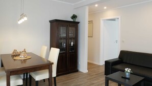 A dining area with a wooden table and chairs, a cabinet with glass doors, a black sofa, and a small table with a remote control. - Vacation apartment by the Baltic Sea - Apartment Kapitän 3 (Zinnowitz)