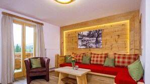Une pièce chaleureuse avec un mur en bois, un canapé rouge, un fauteuil en cuir marron et une table basse en bois sur laquelle est posé un vase de fleurs.