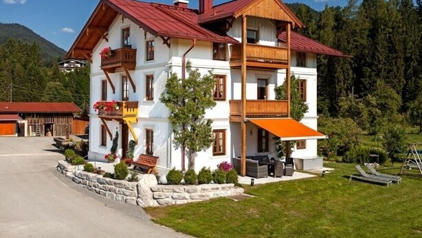Un chalet à deux étages, avec un toit rouge, des balcons en bois et des fondations en pierre.