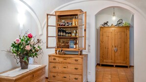 Een houten kast met open planken waarop verschillende flessen en potten staan, een vaas met bloemen en een houten dressoir.
