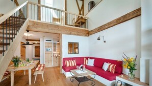 Een ruime woonkamer met een rode bank, houten vloer, een eettafel en een trap naar een hoger gelegen verdieping.