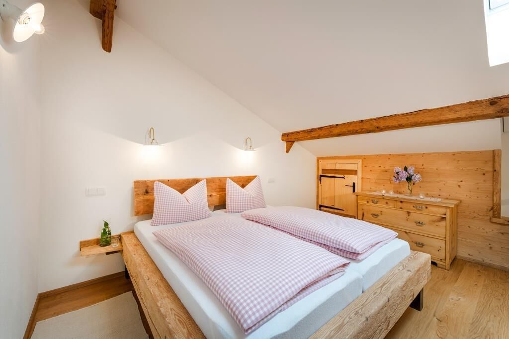 A bedroom with a wooden bed frame, two bedside tables, a wooden dresser, and a window with a view.