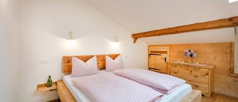 A bedroom with a wooden bed frame, two bedside tables, a wooden dresser, and a window with a view.