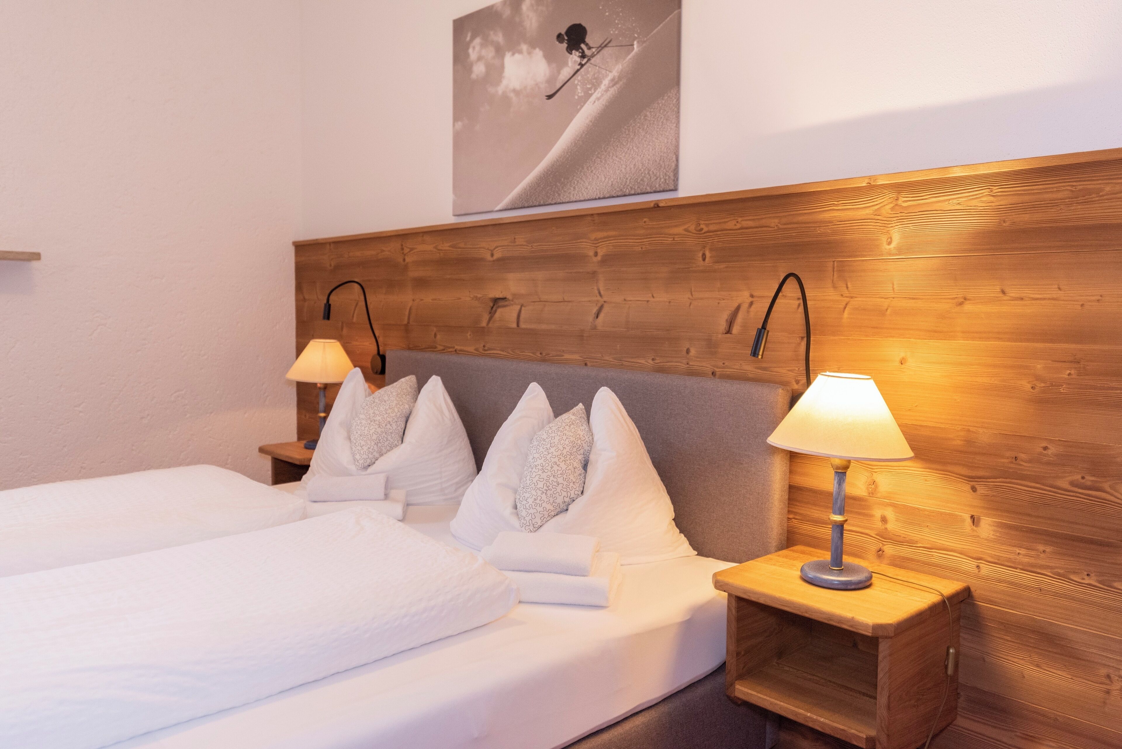 Una cama doble con sábanas y almohadas blancas, dos mesitas de noche con lámparas y un cabecero de madera.
