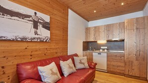 A cozy living area with a red leather sofa, wooden walls, and a kitchen with wooden cabinets. - "DEPENDANCE BERGSTÜBERL" 102 (Reit im Winkl)