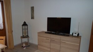 A living room with a television on a wooden cabinet, a small table with a candle, and a wall-mounted decoration. - Three-room vacation apartment, 40m², bedroom, children's room, living room, kitchenette, balcony (Reit im Winkl)