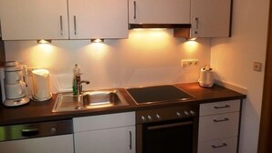 A compact kitchen with white cabinets, a stainless steel sink, a built-in oven, and a coffee maker. - Three-room vacation apartment, 40m², bedroom, children's room, living room, kitchenette, balcony (Reit im Winkl)