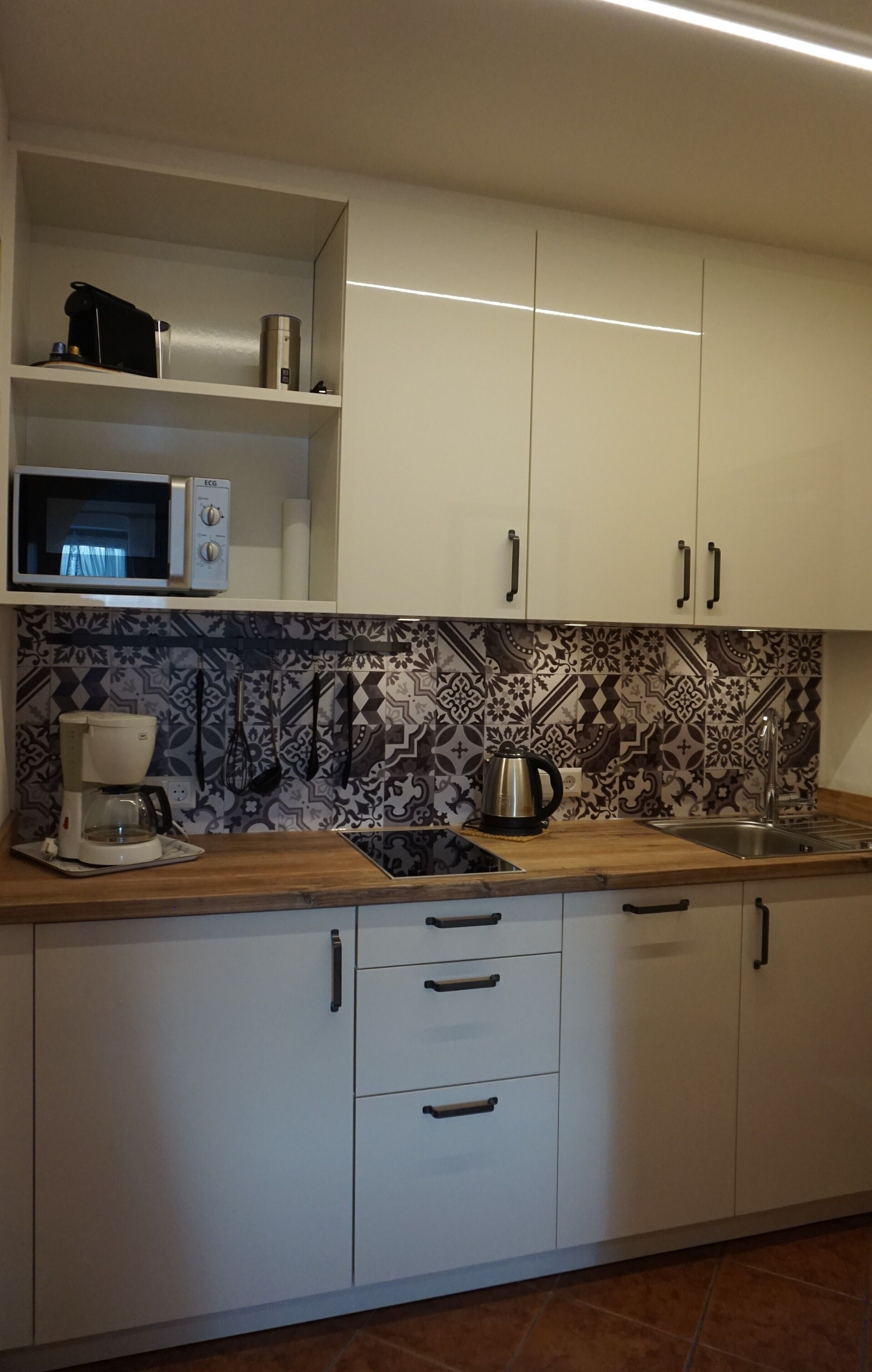 A kitchen with white cabinets, a patterned backsplash, a coffee maker, a kettle, and a microwave.