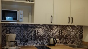 A kitchen with white cabinets, a patterned backsplash, a coffee maker, a kettle, and a microwave. - (08) Ein-Raum-Ferienwohnung 33qm, Dusche/WC, Koschnische, Balkon (Reit im Winkl)