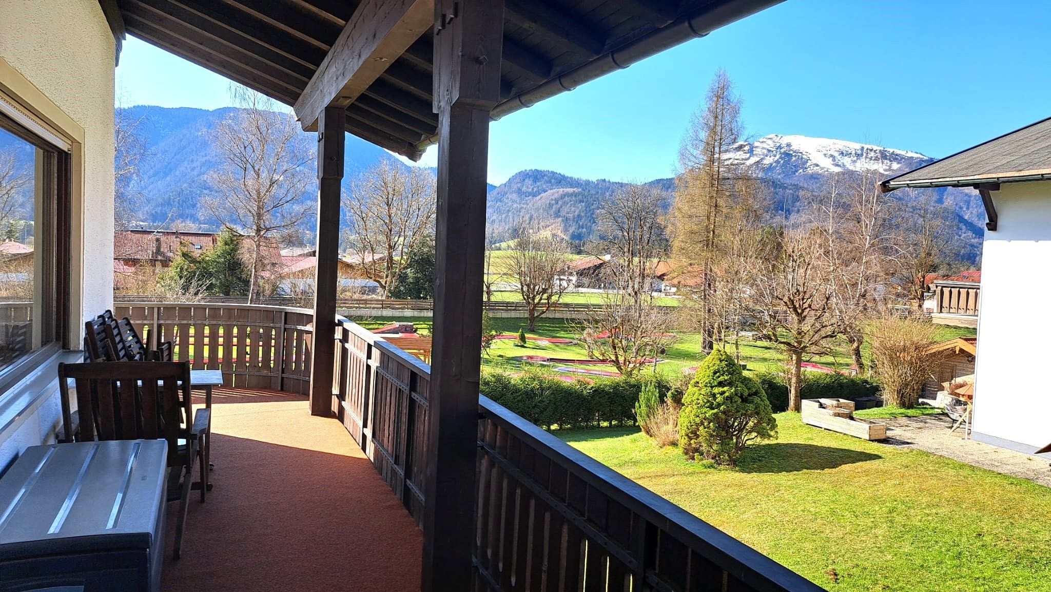 Un balcon offrant une vue sur un paysage montagneux, une terrasse en bois et une table avec des chaises.