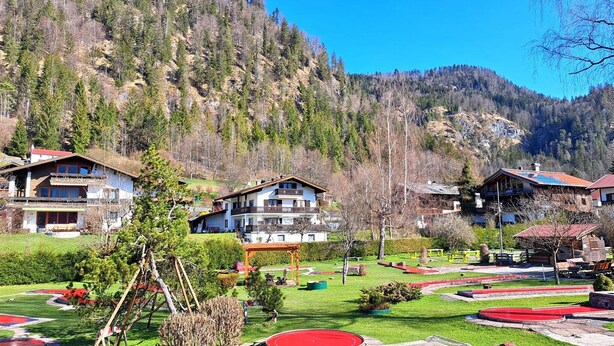 A mountain resort with multiple chalet-style buildings, a well-maintained garden, and a clear view of the surrounding forested hills.