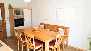 A compact kitchen with a built-in oven and microwave, a wooden dining table with four chairs, and a bench with cushions.