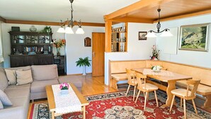 A cozy living room with a sofa, a wooden dining table with chairs, a coffee table with a vase, and a patterned rug.