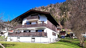 A multi-story building with balconies, a sign reading 'Glück im Winkel', and a mountainous backdrop.
