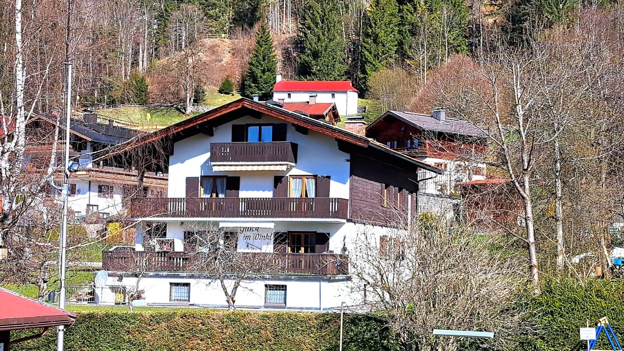 A multi-story building with a balcony, a red roof, and a sign that reads "Gästehaus im Dinkel".