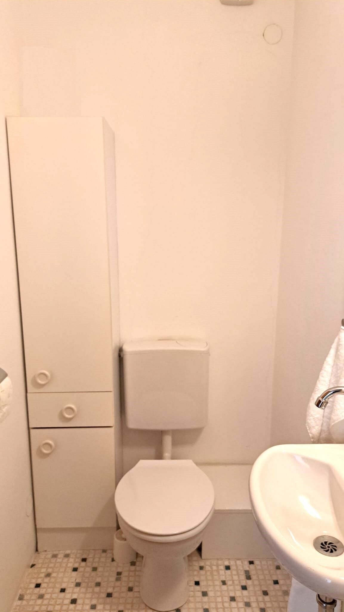 A small, white bathroom with a toilet, a sink, and a cabinet with drawers.