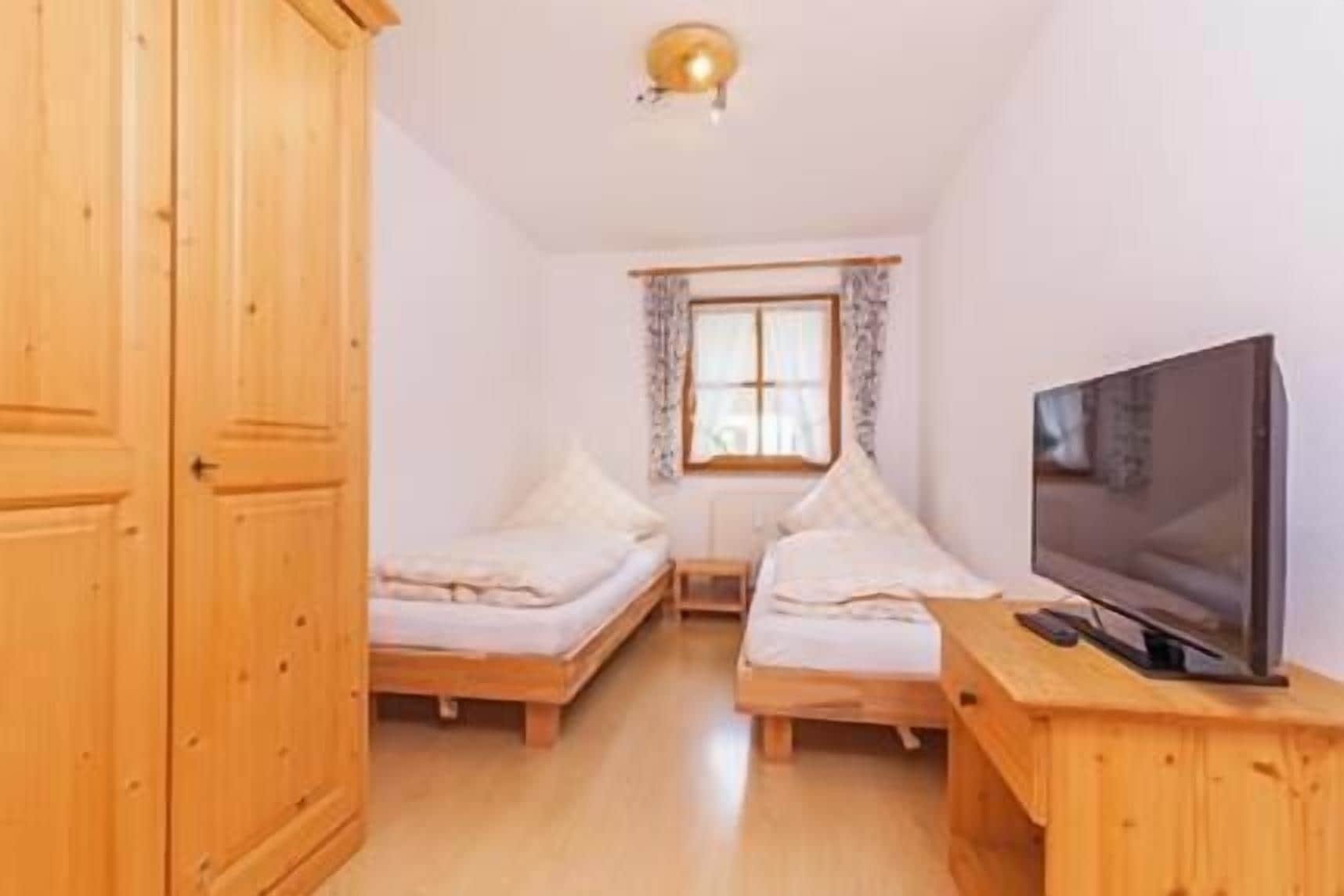 Een kleine kamer met twee eenpersoonsbedden, een televisie op een houten standaard en een raam met gordijnen.