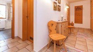 Un pasillo con puertas de madera, una silla de madera, una mesita con lámpara y un radiador al fondo.