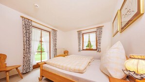 Un dormitorio con una cama de madera, dos ventanas con cortinas, una mesita de noche y una lámpara.