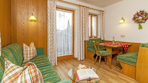 A cozy living room with a green sofa, a dining table with chairs, and a glass coffee table with a book. - Ferienwohnung (5) (Reit im Winkl)