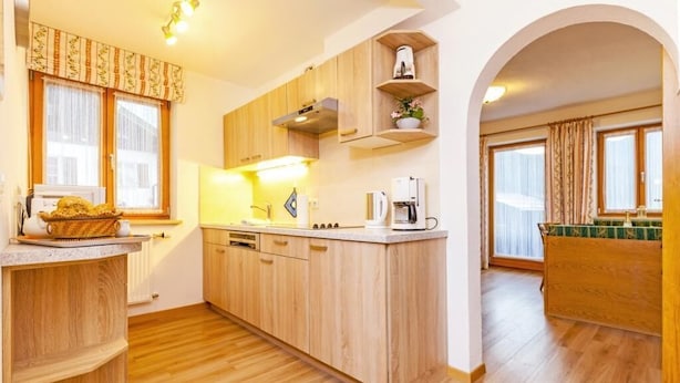 A modern kitchen with wooden cabinets, a central island, and built-in appliances. - Ferienwohnung (5) (Reit im Winkl)