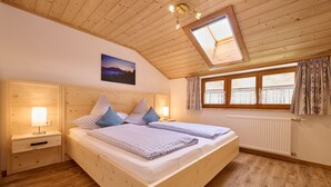 Ein Schlafzimmer aus Holz mit einem Bett, zwei Nachttischen, einem Fenster mit Vorhängen und einem Dachfenster.