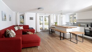 A modern living room with a red sofa, wooden benches, and a kitchen area with a central island. - Ferienwohnung "Geniessen" für 2-8 Personen, 4 Schlafzimmer, 2 Bäder (Breitbrunn am Chiemsee)