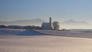 Paisaje nevado con una iglesia y montañas al fondo.