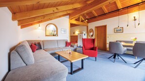 A modern living room with a wooden ceiling, a grey sofa, a red armchair, and a small table with two glasses. - 10 Apartment type D 71 sqm, balcony, 2 bedrooms, living room, max 4 p, WLAN (Ruhpolding)