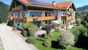 A two-story chalet with a red-tiled roof, balconies with flower boxes, and a paved driveway. - 10 Apartment type D 71 sqm, balcony, 2 bedrooms, living room, max 4 p, WLAN (Ruhpolding)