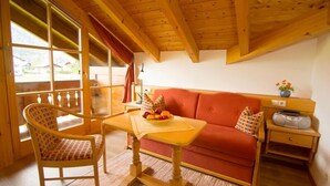 Une pièce chaleureuse avec un plafond en bois, un canapé rouge, une table en bois sur laquelle se trouve un panier de fruits et un fauteuil.