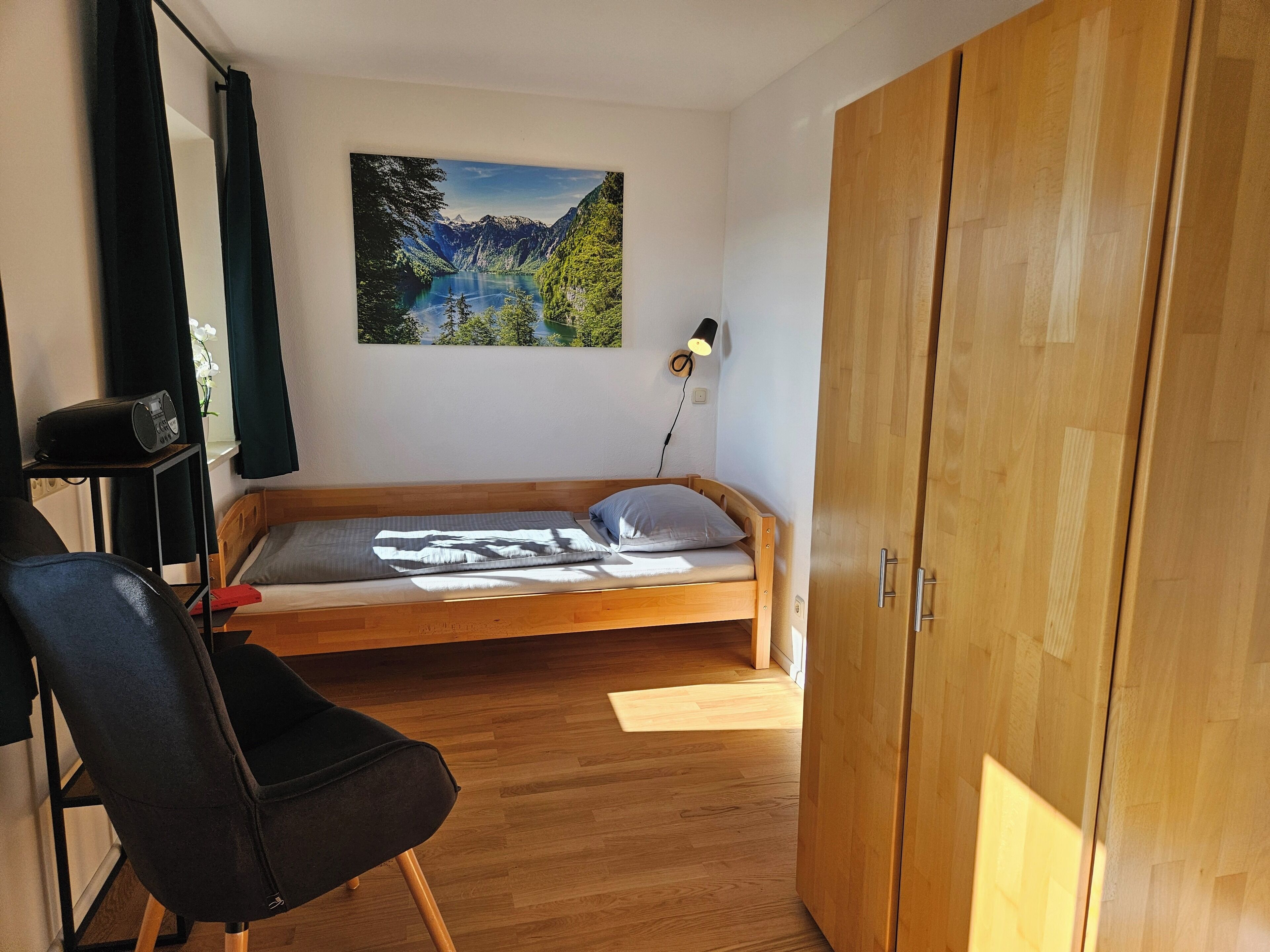 Un dormitorio con una cama de madera, una silla, un escritorio con lámpara y un cuadro de un paisaje en la pared.