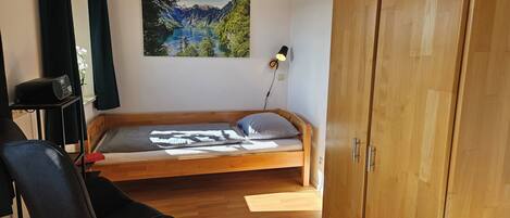 Un dormitorio con una cama de madera, una silla, un escritorio con lámpara y un cuadro de un paisaje en la pared.