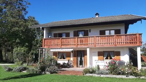 A two-story building with a balcony, a covered patio, and a garden area. - holiday flat (Gstadt am Chiemsee)