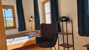 A room with a bed, a chair, a shelf, and a window. - holiday flat (Gstadt am Chiemsee)