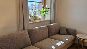 A modern living room with a brown sofa, a small round table, and a window with plants. - holiday flat (Gstadt am Chiemsee)
