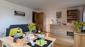 Una sala de estar moderna con comedor, que incluye un sofá, una mesa de madera con comida y bebidas, una estantería y una puerta que da a otra habitación.