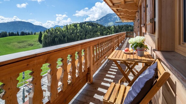 A wooden balcony with a view of a green field and mountains.
