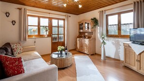 A spacious living room with a wooden ceiling, a sofa, a coffee table, and a TV on a cabinet.