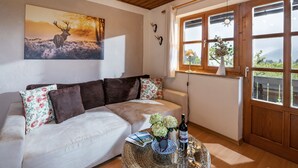 A cozy living room with a white sofa, a wooden ceiling, a painting of a deer, and a large window with a view of greenery.