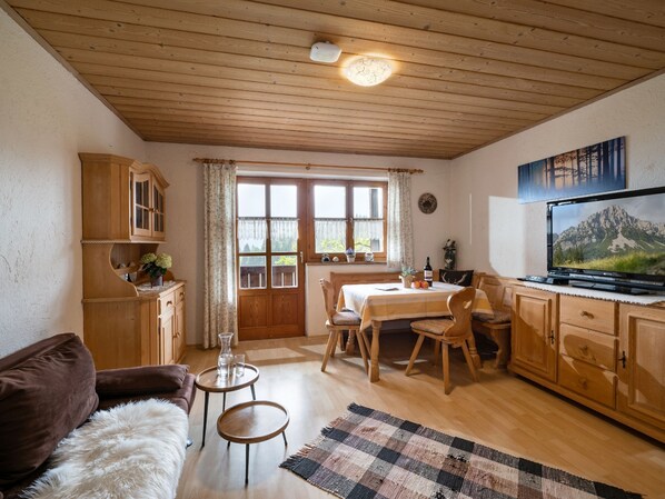 A cozy living room with wooden furniture, a dining area, and a TV on the wall.