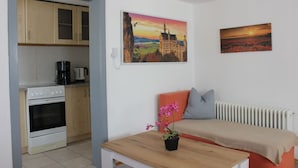 Un espace de vie compact comprenant un coin cuisine, un canapé, une table basse et deux tableaux accrochés au mur.