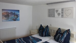Une chambre à coucher avec un lit, des oreillers, une table de chevet, une lampe, un radiateur et des œuvres d’art murales.