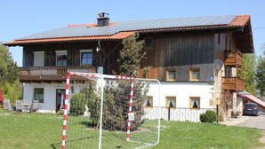 Une maison rustique en bois, dotée d’un toit équipé de panneaux solaires, d’un but de football entouré d’une clôture et d’un balcon.