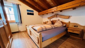 Un lit en bois avec une tête de lit, une table de chevet et une petite table de nuit, dans une pièce au plancher de bois et au plafond en pente.