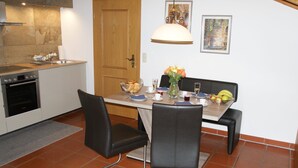 Un coin repas avec une table en bois, des chaises noires, un vase de fleurs et un saladier de fruits.