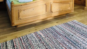 Una cama de madera con almohadas verdes, un cabecero de madera, un cuadro de un paisaje, un espejo y una puerta de madera.