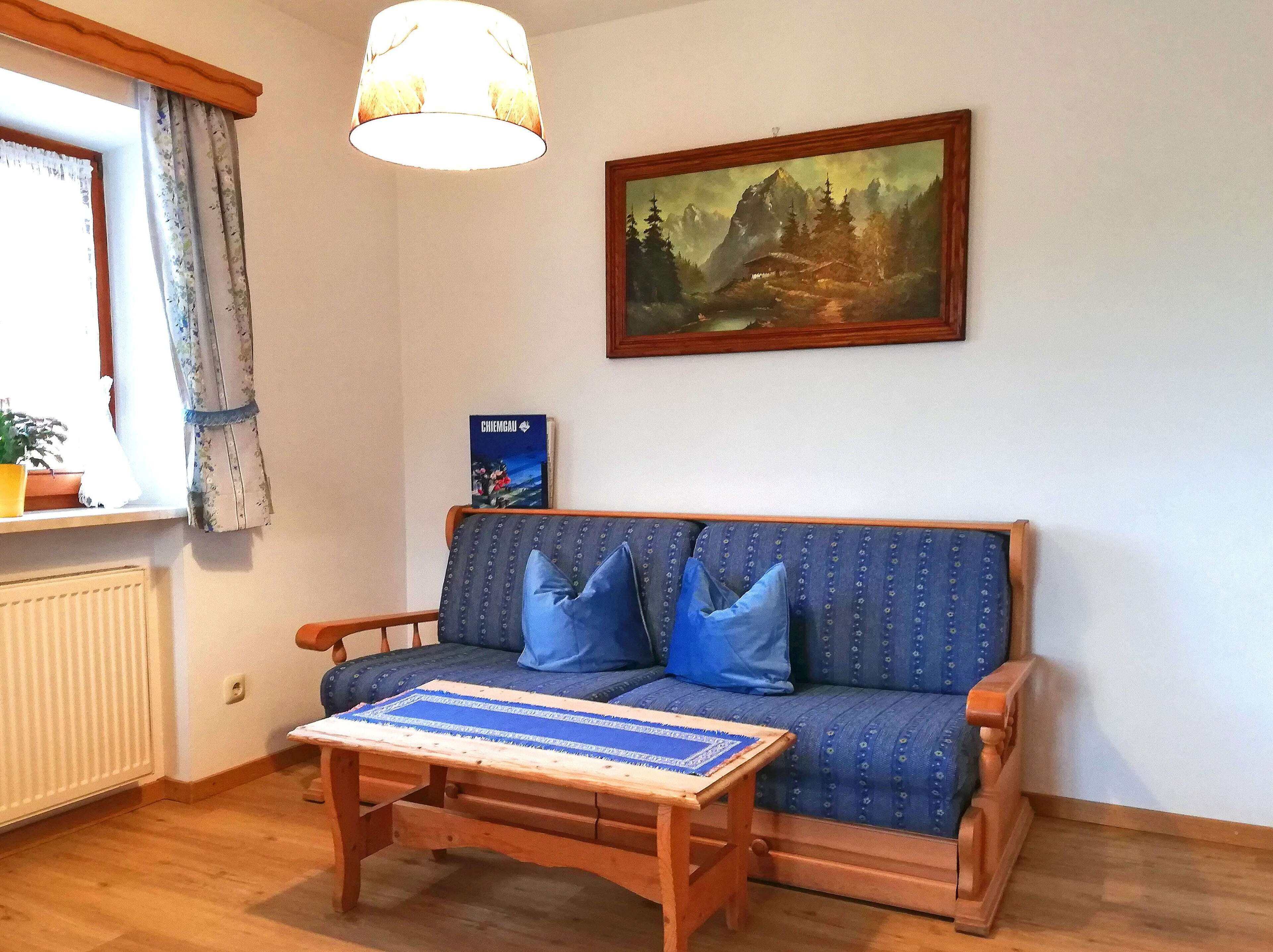 A cozy living room with a blue sofa, a wooden coffee table, and a painting on the wall.