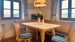 Un comedor con una mesa y sillas de madera, una araña y vistas a través de las ventanas.