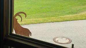 Vista a través de una ventana: un campo verde, una cadena montañosa y un edificio a lo lejos.